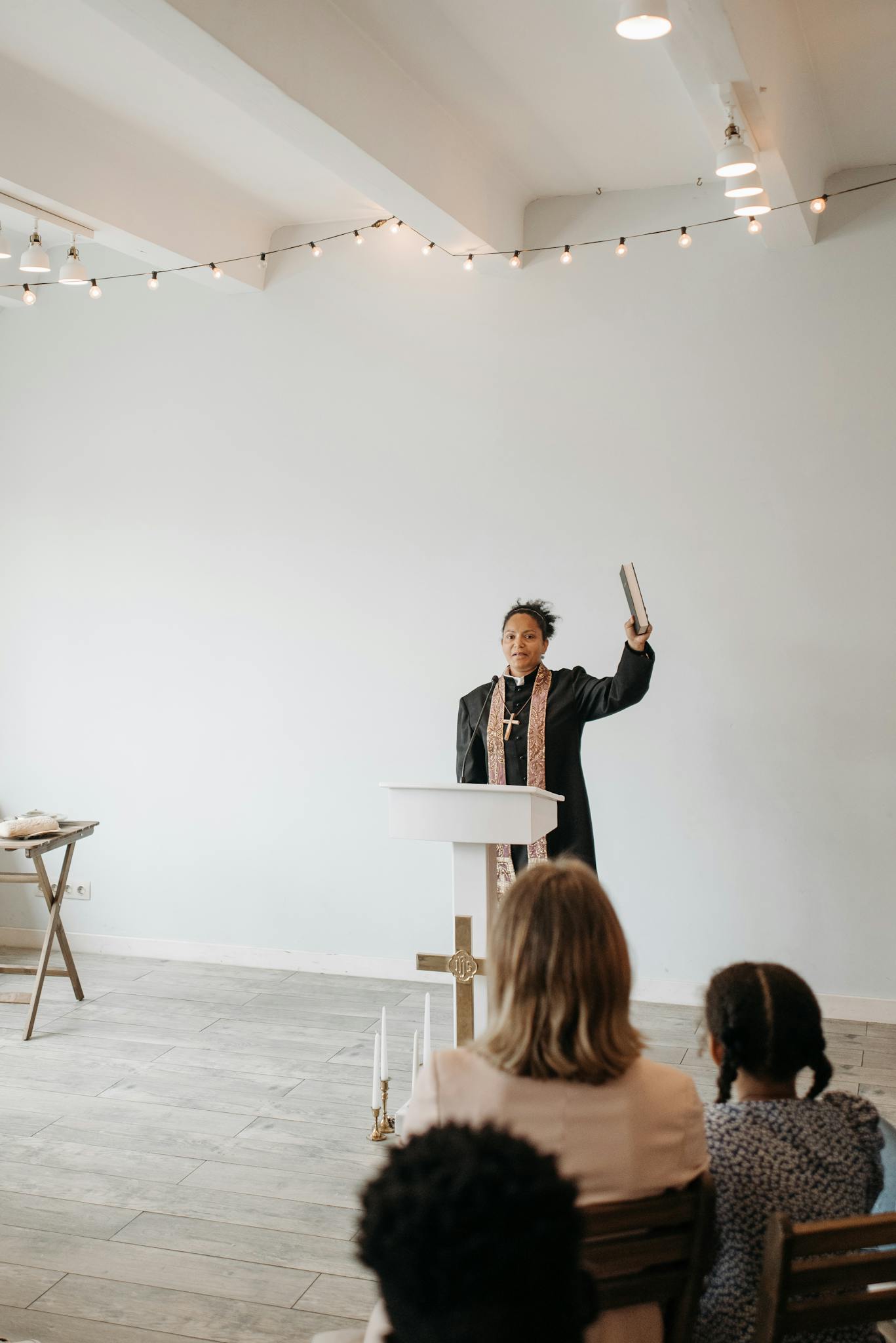 A female pastor delivering a sermon to a small congregation in a minimalist church interior.