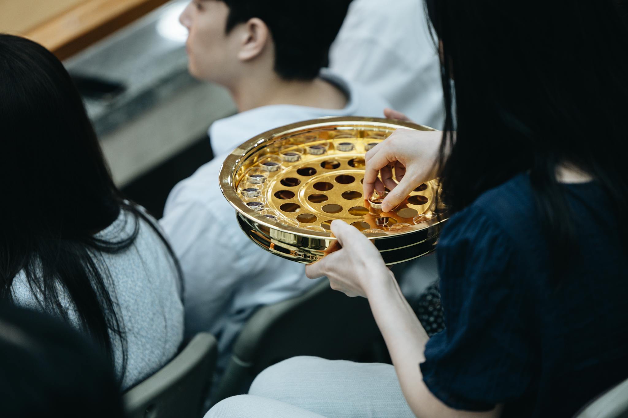 A golden communion plate is passed during a church service, reflecting the act of worship.