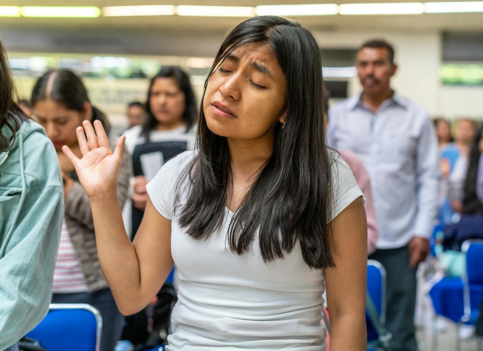 A young woman with closed eyes prays during a worship service in a community setting.
