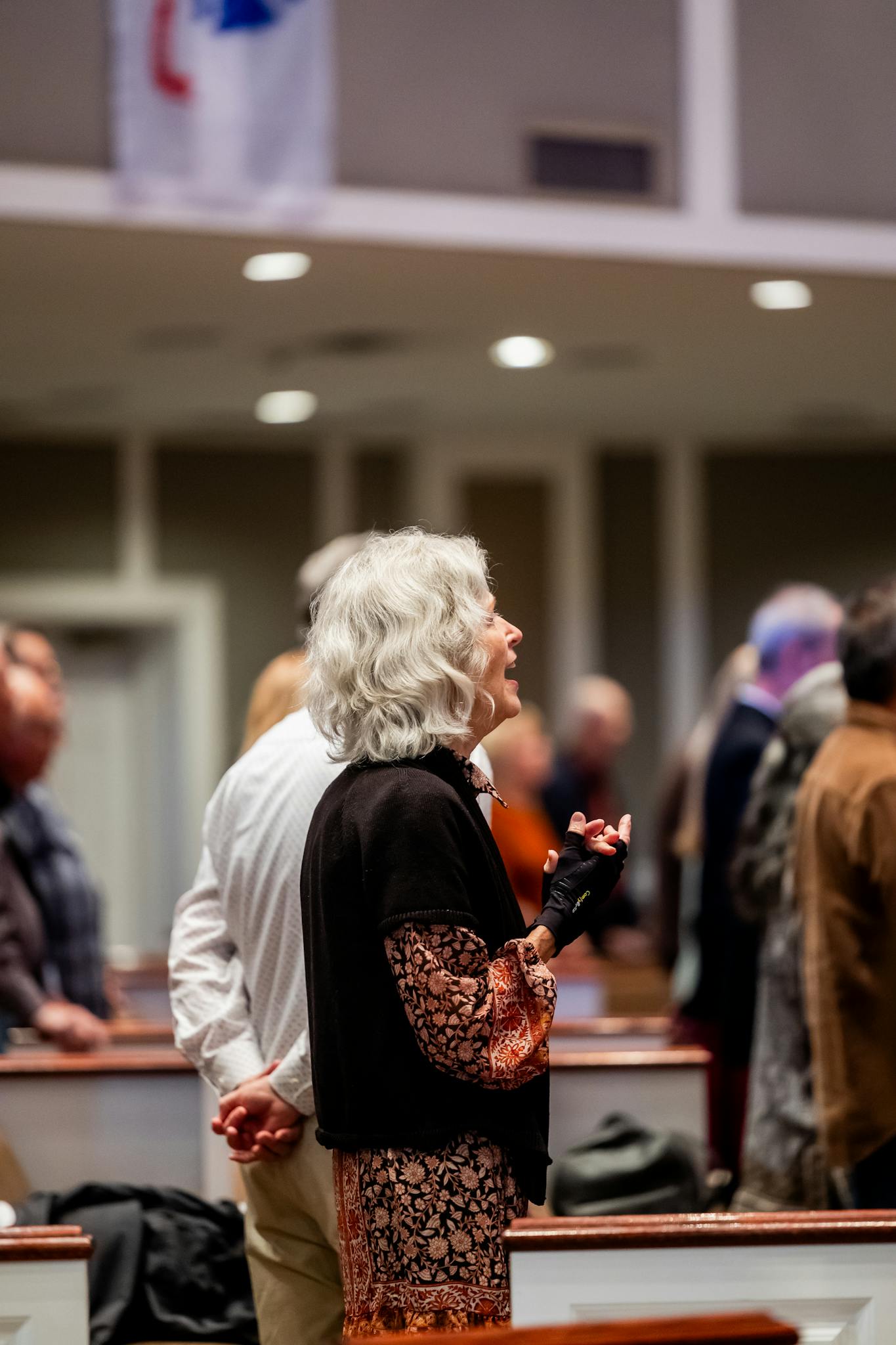 Senior woman singing during a church service with a diverse congregation in attendance.